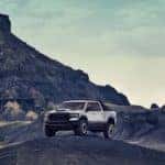 A silver 2021 Ram 1500 TRX is perched atop a hill in front of mountains.
