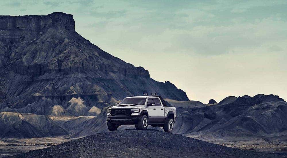 A silver 2021 Ram 1500 TRX is perched atop a hill in front of mountains.