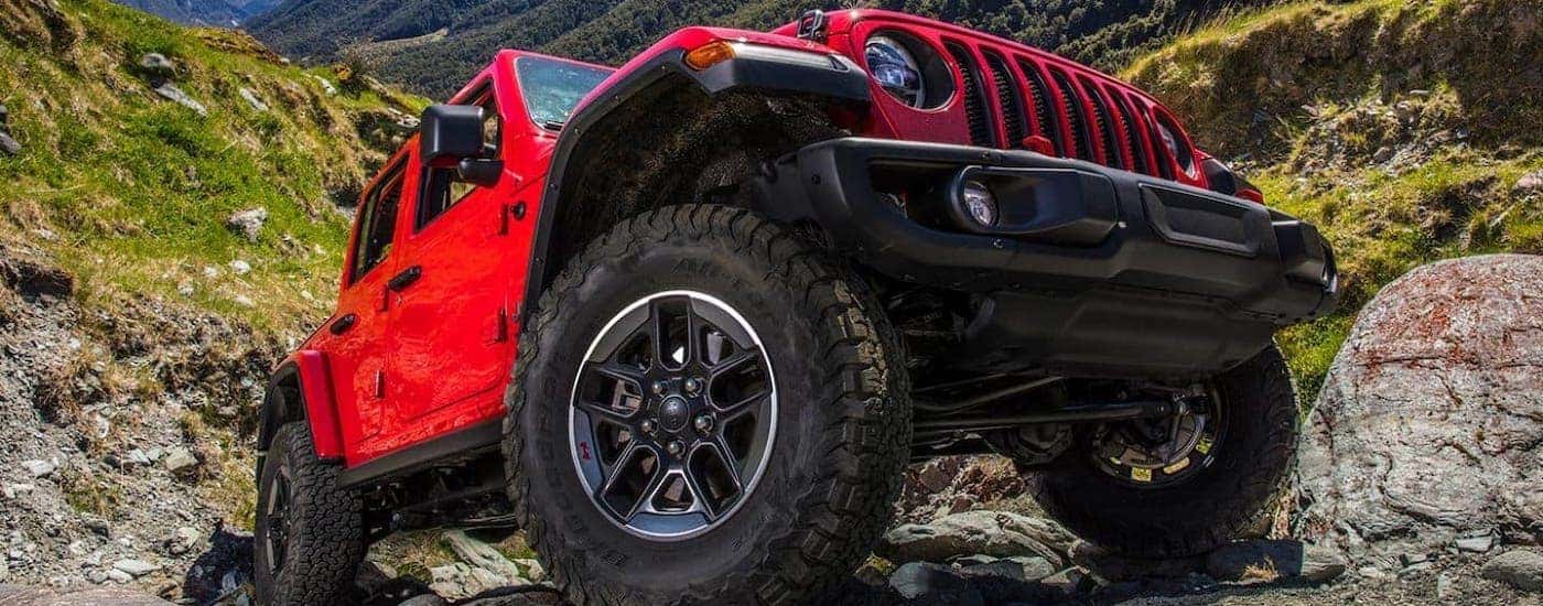 A closeup shows the tire on a red 2021 Jeep Wrangler Unlimited that is climbing over a rock.