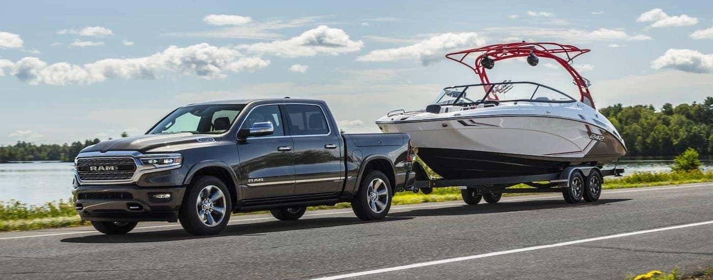 A gray 2021 Ram 1500 is towing a boat on a road in front of a river.