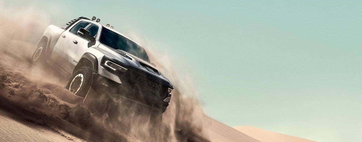 A highly anticipated Ram truck, a silver 2021 Ram 1500 TRX, is shown kicking up sand on a dune.