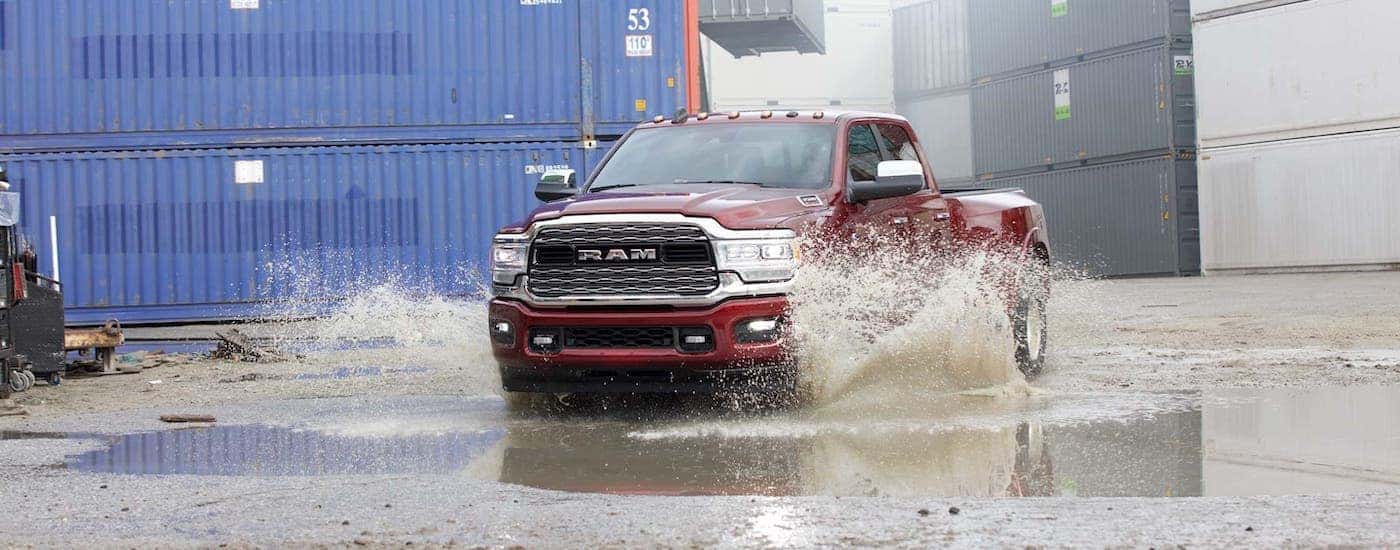 A red 2021 Ram 3500 is driving through a puddle in front of shipping containers.
