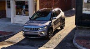 A grey 2021 Jeep Compass is pulling out of a side street in a city.