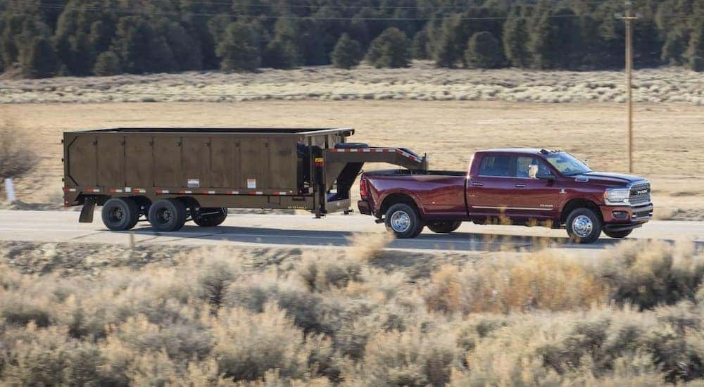 A red 2021 Ram 3500 is towing a black trailer past a field.