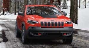 A red 2020 Jeep Cherokee, a popular used Jeep for sale in Cincinnati, is driving on a snow-lined road.