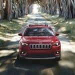 A red 2020 Jeep Cherokee is driving on a narrow road lined with large trees.