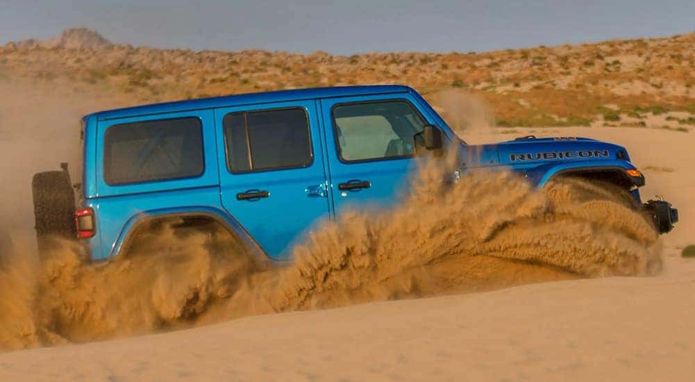 A blue 2021 Jeep Wrangler Rubicon 392 is off-roading in sand, shown from the side.