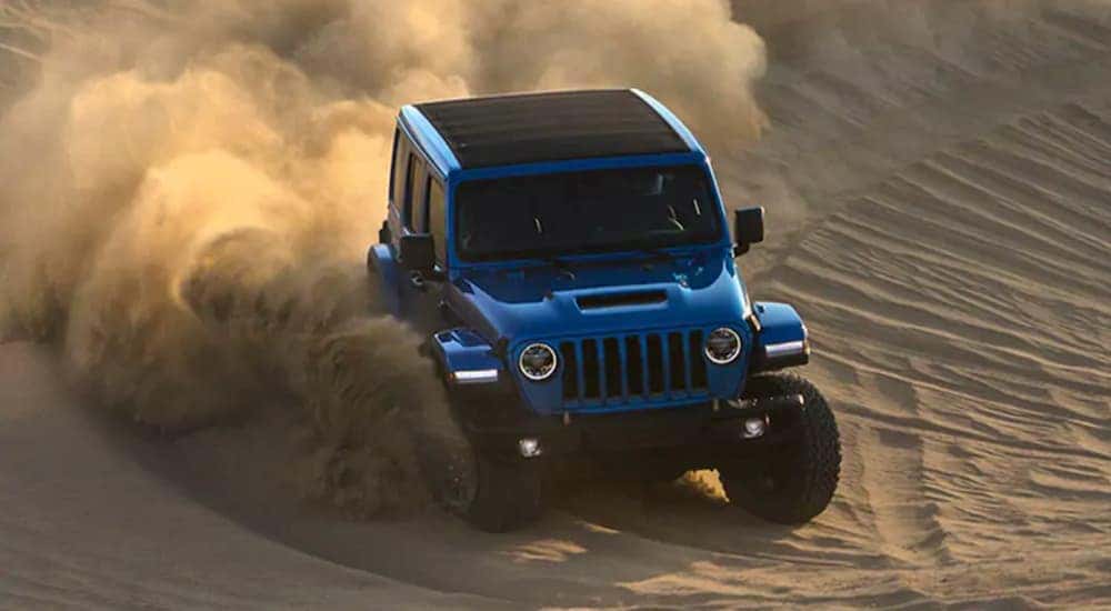 A blue 2021 Jeep Wrangler Rubicon 392 is off-roading in sand.