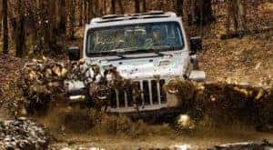 A white 2021 Jeep Wrangler is off-roading in the mud.