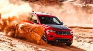 A red 2021 Jeep Grand Cherokee Trailhawk is kicking up sand while driving on a dune.