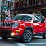 A popular model for many Jeep dealers in Ky, a red 2021 Jeep Renegade, is driving through the city over a crosswalk.