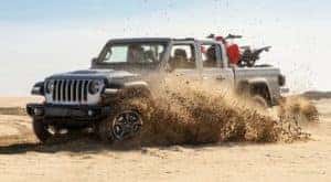 A silver 2021 Jeep Gladiator Rubicon is off-roading in sand with a dirt bike in the bed.