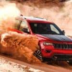 A red 2021 Jeep Grand Cherokee is off-roading in sand.