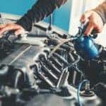 A close up shows a mechanic with a blue canister filling oil after a recent service.