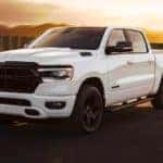 A white 2021 Ram 1500 Big Horn Night Edition is shown driving down the road at sunset after leaving a Ram dealer in Cincinnati.