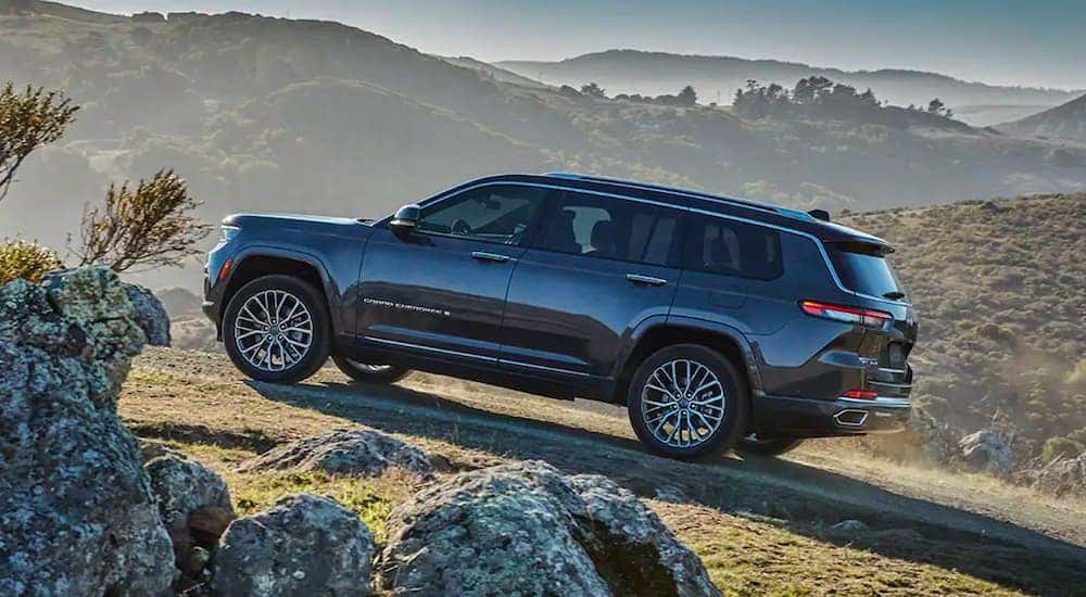 A dark grey 2021 Jeep Grand Cherokee L is shown from the side driving up a rocky path.