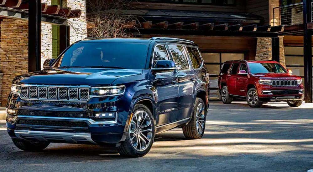 A blue and a red 2022 Grand Wagoneer are parked in front of a modern cabin.