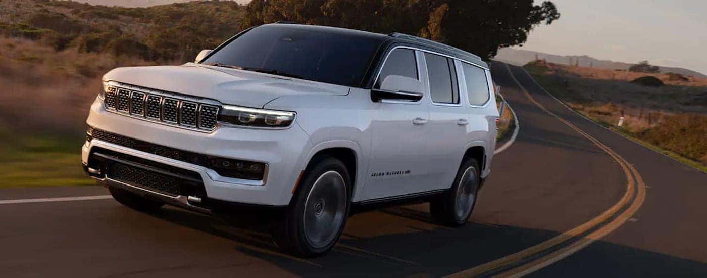 A white 2022 Grand Cherokee Wagoneer is driving on a snow covered road past pines after leaving a Cincinnati Jeep dealer.
