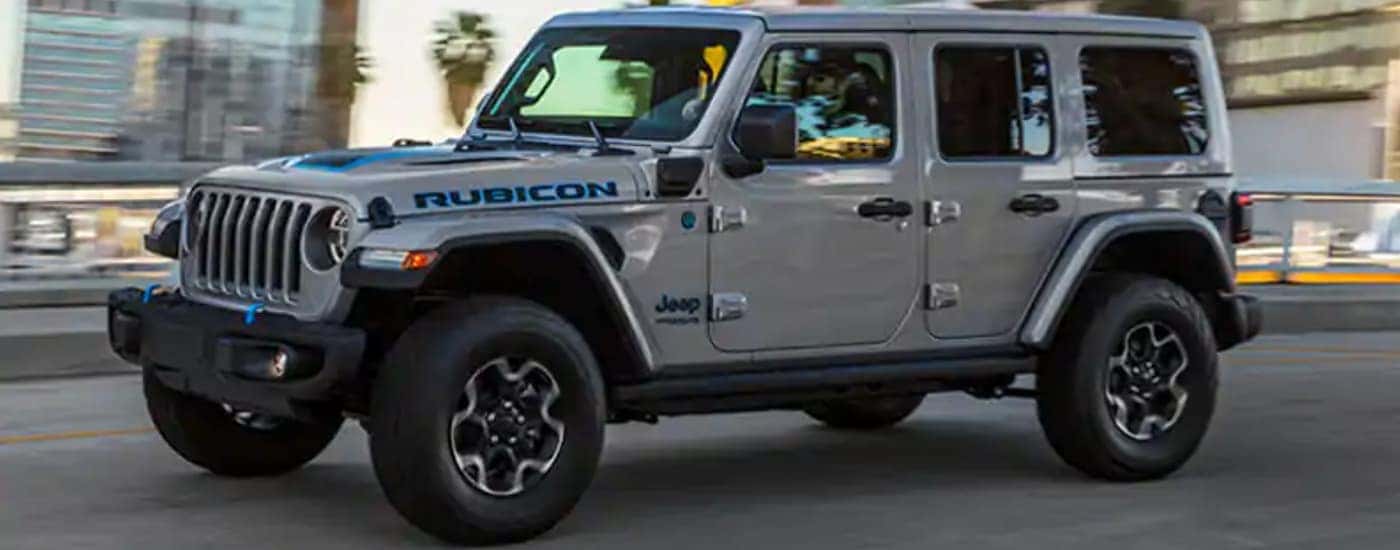 A silver 2021 Jeep Wrangler Unlimited 4xe is driving on a city street.