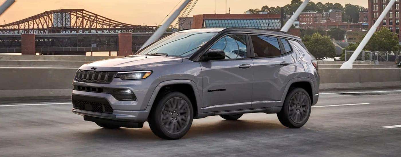 A grey 2022 Jeep Compass is shown from the side driving over a bridge after leaving a Covington Jeep dealership.