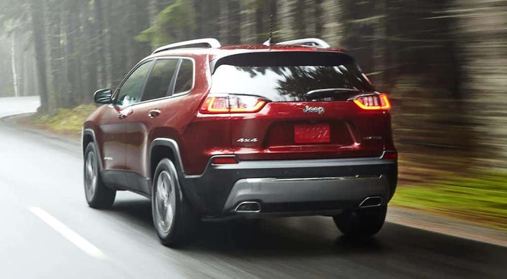 A red 2021 Jeep Cherokee is shown from the back driving down a forest road.