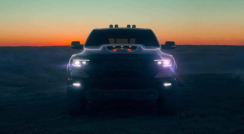 A black 2021 Ram 1500 TRX is shown from the front with its lights on at dusk.