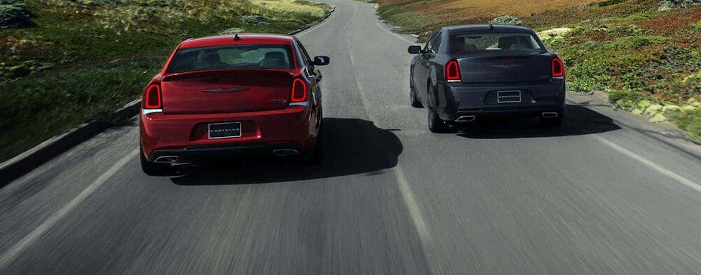 A red and a grey 2021 Chrysler 300 are driving next to each other on a two lane road.