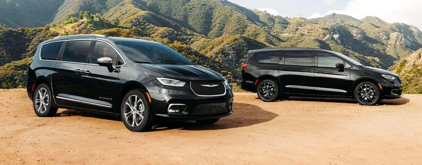 Two black 2021 Chrysler Pacificas are parked on dirt in front of mountains.