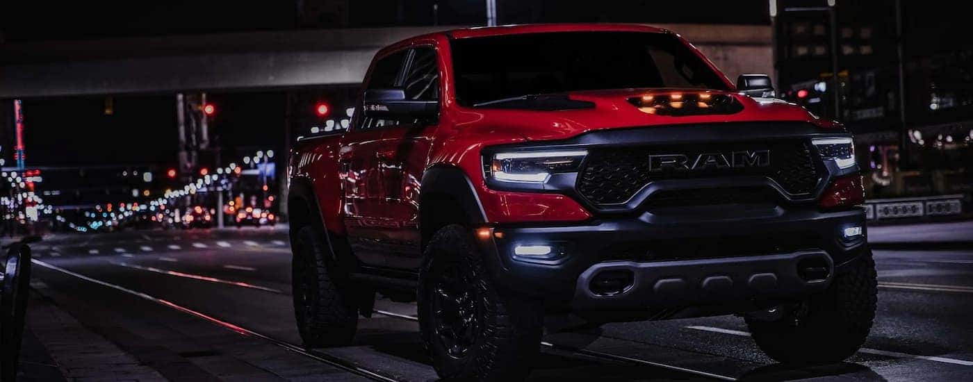 A red 2022 Ram 1500 TRX is shown driving on a city highway at night.