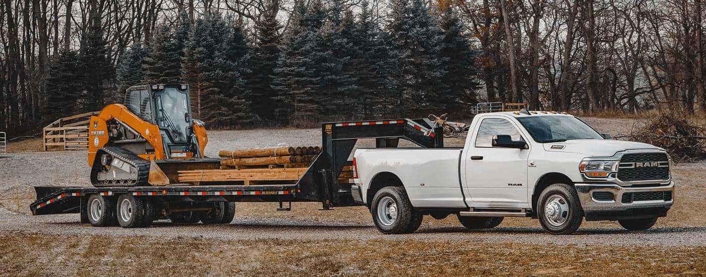 A white 2022 Ram 3500 is shown towing heavy machinery on a trailer.