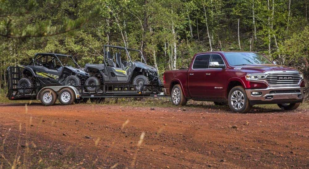 A red 2021 Ram 1500 is parked on a dirt trail, in front of trees, with a side by side on a trailer after leaving a Cincinnati used truck dealer.