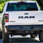 A white 2020 Ram 1500 Rebel is shown from the rear driving down an empty road.