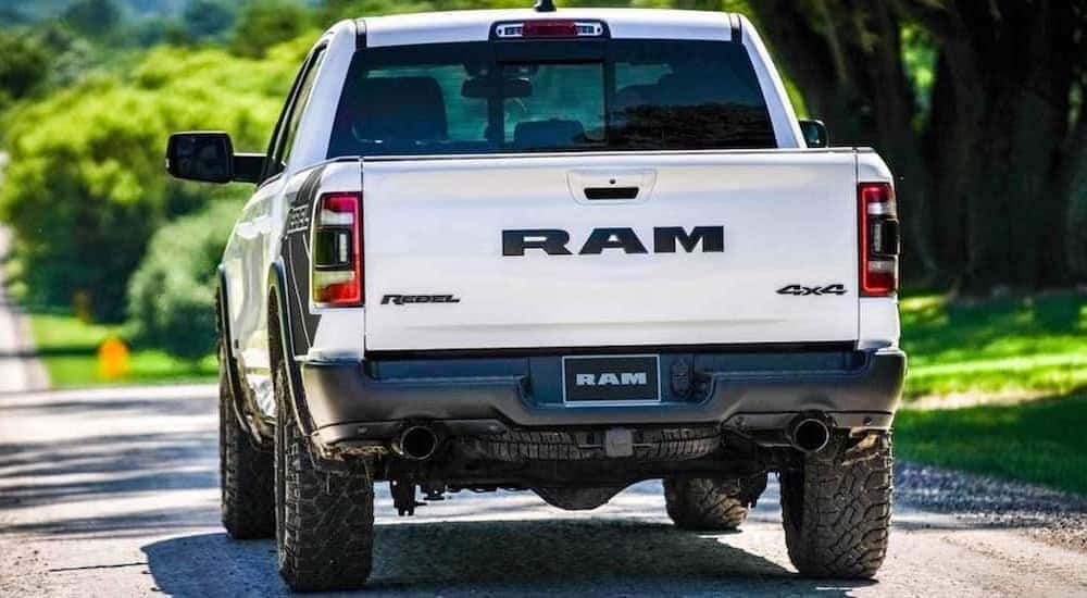 A white 2020 Ram 1500 Rebel is shown from the rear driving down an empty road.