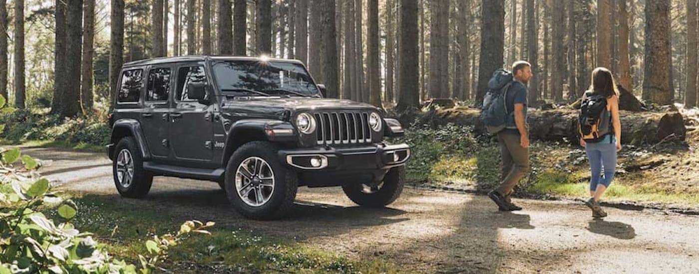 A grey 2020 Jeep Wrangler Unlimited is parked on a trail next to two hikers.