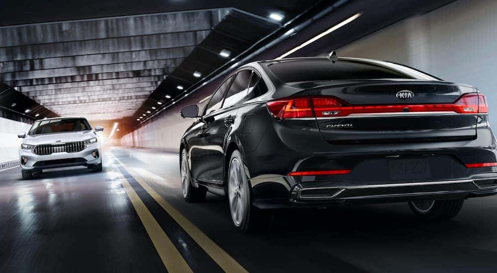 A white and a black 2020 Kia Cadenza are shown passing each other in a tunnel.