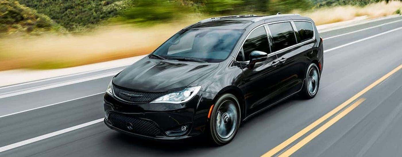 A black used 2020 Chrysler Pacifica is driving down a two lane road after leaving a used car dealer…