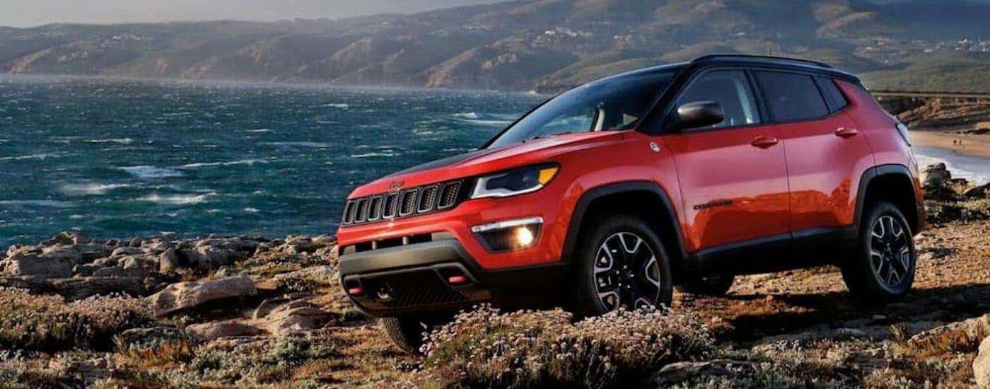 A red 2020 Jeep Compass Trailhawk is parked next to the ocean.