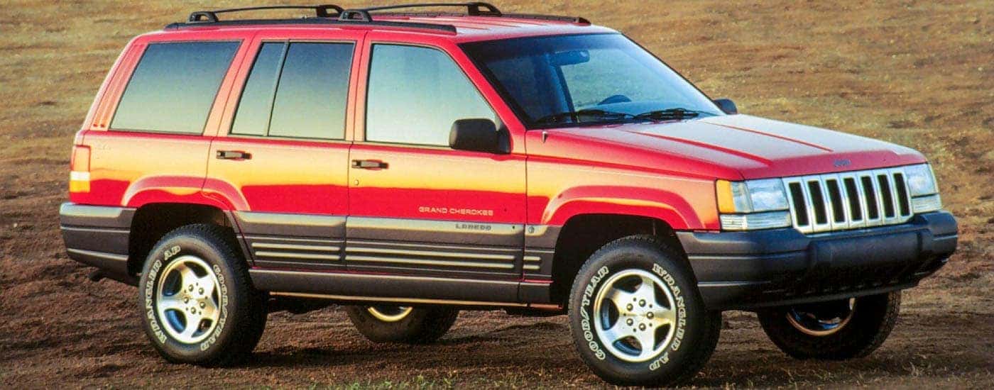 A red 1996 Jeep Grand Cherokee Laredo is shown from the side parked in a field.