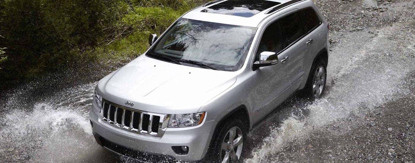 A silver 2013 Jeep Grand Cherokee is shown from a high angle splashing through water.