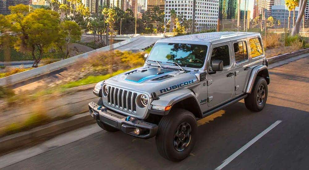 A silver 2021 Jeep Wrangler 4xe is shown driving through a city after visiting a Jeep Grand Cherokee dealer.