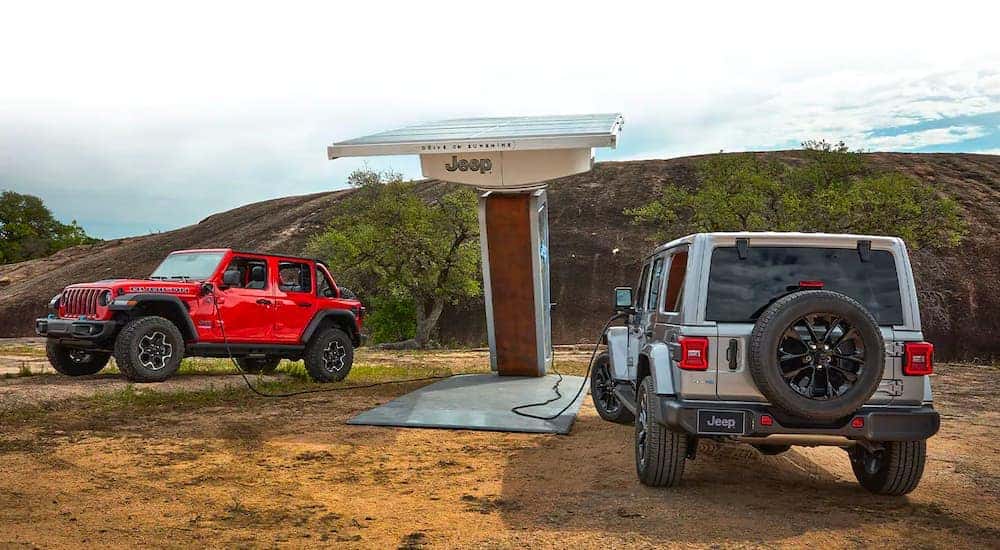 A red and a silver 2021 Jeep Wrangler 4xe Rubicon Unlimited are shown at a charging station.