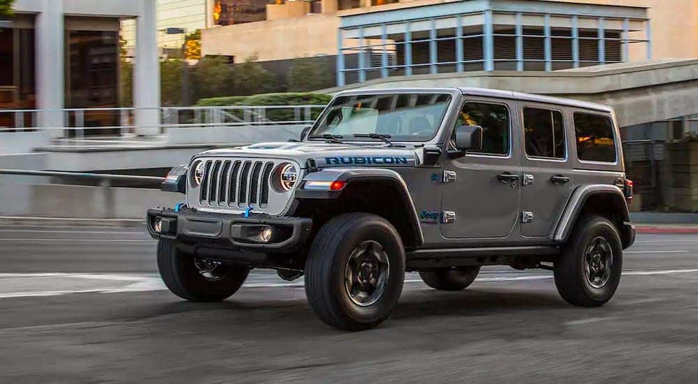 A grey 2021 Jeep Wrangler 4xe Rubicon Unlimited is shown driving through a city after visiting a Covington Jeep dealership.