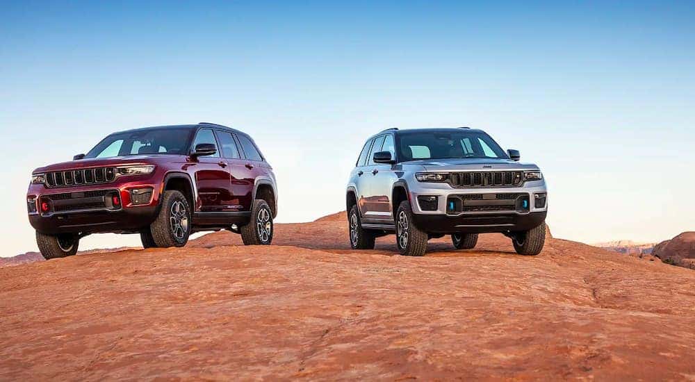A burgundy 2022 Jeep Grand Cherokee 4xe and a silver Cherokee 4xe are shown parked on a rock face.