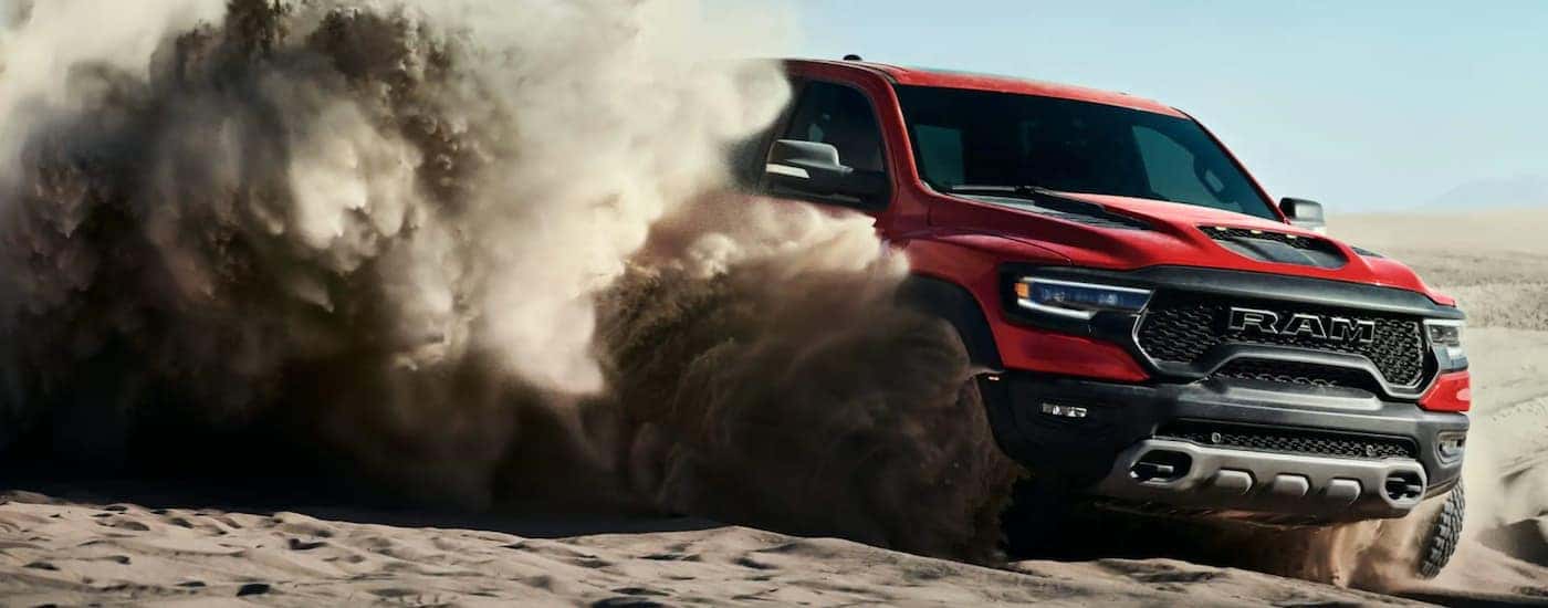 A red 2021 Ram 1500 TRX is shown from the side off-roading through a sandy desert.