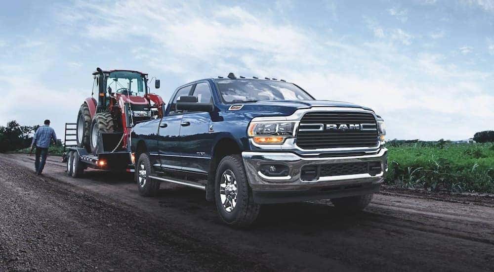 A blue 2021 Ram 2500 is shown towing a red tractor on a dirt road.