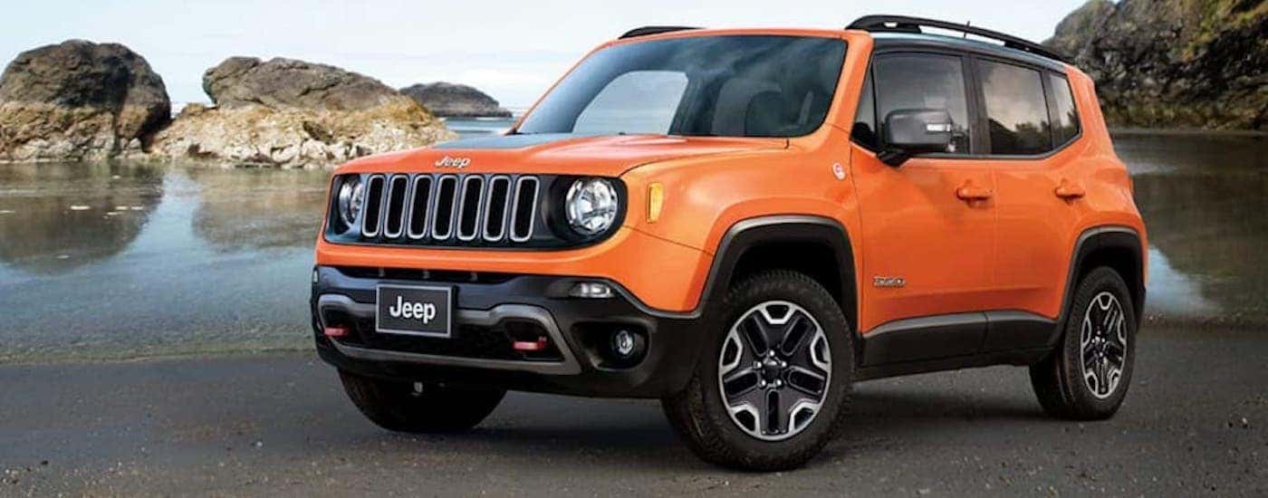 An orange 2018 Jeep Renegade is shown parked by a body of water.