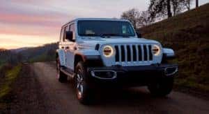 A white 2019 certified pre-owned Jeep Wrangler is shown driving on a road during sunset.