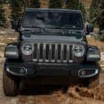 A grey 2019 certified pre-owned Jeep Wrangler is shown from the front off-roading on a muddy trail.