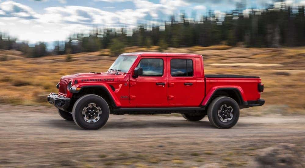 A red 2020 Jeep Gladiator is shown from the side driving on a dirt road.