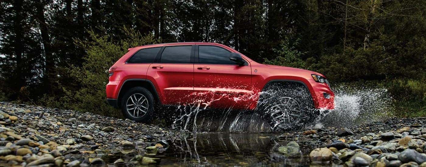 A red 2020 Jeep Grand Cherokee is shown from the side driving through a puddle.